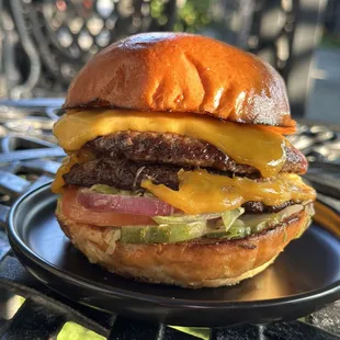 two angus beef patties, ground in-house, cheddar cheese, remoulade, shredded iceberg lettuce, tomato, house pickles, and red onion on a brio