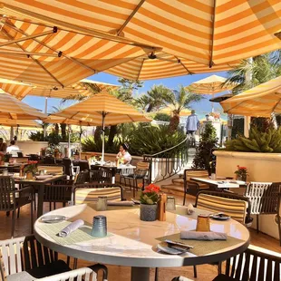 tables and chairs with yellow and white striped umbrellas