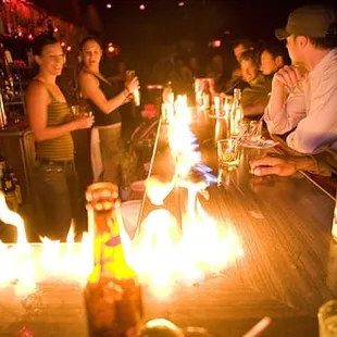 a group of people standing around a bar with candles on it
