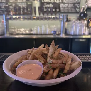 a bowl of fries with a side of dipping sauce