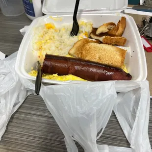 a hot dog, scrambled eggs, and toast in a plastic container