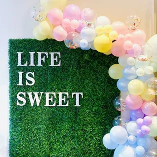a green wall with balloons and the words life is sweet