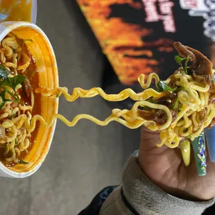 a person holding a cup of noodles