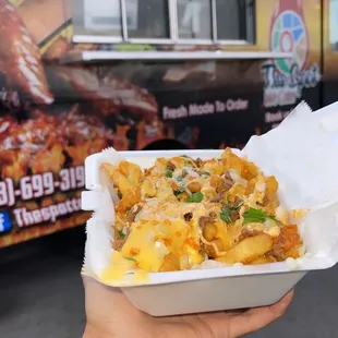a person holding a container of food in front of a food truck