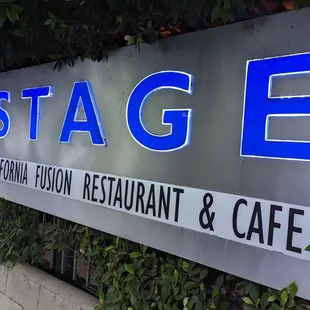 Outside the front of The Stage, this neon + metal sign is surrounded by greenry; the same aesthetic continues inside the restaurant.