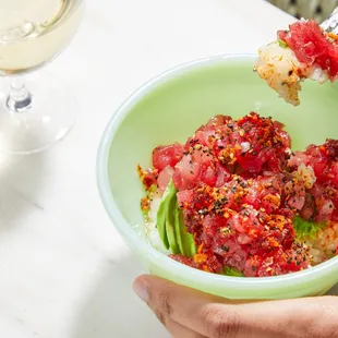 a person holding a bowl of food and a glass of wine