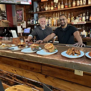 two men sitting at a bar with plates of food