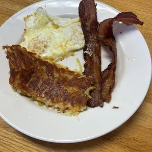 Two over-easy eggs, with two slices of bacon and a deliciously seasoned hash brown.