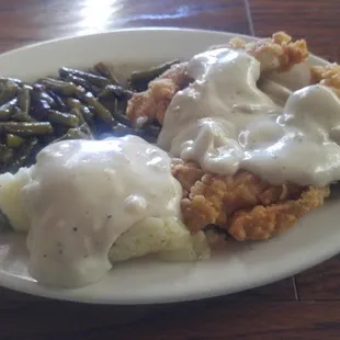 a plate of food with gravy, mashed potatoes and green beans