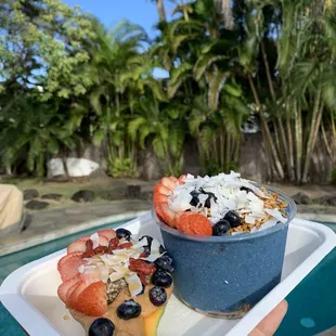 a person holding a plate of fruit and yogurt