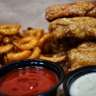 a pile of fried wings with dipping sauces