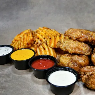 a pile of chicken wings, fries, and sauces