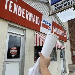 a hand holding a paper cup in front of a restaurant
