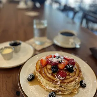 a stack of pancakes with berries and powdered sugar