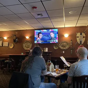 two people sitting at a table watching tv