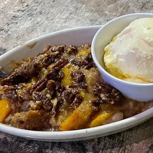 Homemade peach cobber topped with Candied Pecan served with a side of vanilla ice cream.