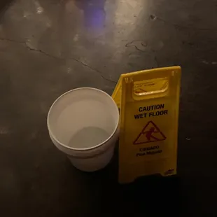 a yellow caution wet floor sign next to a white cup
