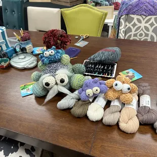 The classroom table with some of our store mascots, The Boogles on display, sitting atop some of our yarns from Kelbourne Woolens