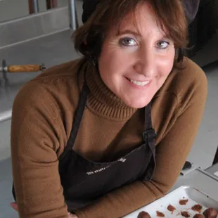 a woman holding a tray of chocolate covered doughnuts