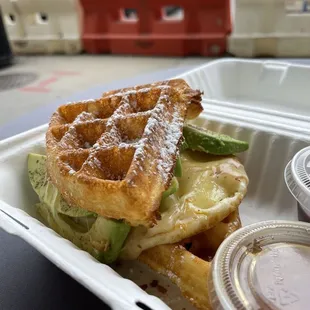 Breakfast waffle sandwich with egg, cheese and avocado. On the side- fruit preserves and maple syrup.