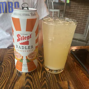 a can of stiegt radler next to a glass of orange juice