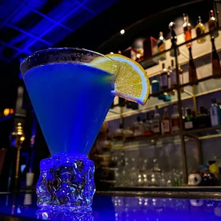 a blue cocktail with a slice of lemon