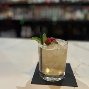 a glass of cocktail with a raspberry garnish