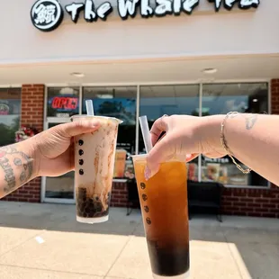 two people holding drinks in front of a coffee shop