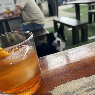 a drink on a table with a man and a dog in the background