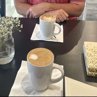 a man sitting at a table with two cups of coffee