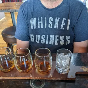 a man sitting at a table with six glasses of whiskey