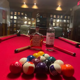 a pool table with pool balls and a bottle of liquor