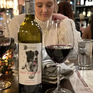 a woman sitting at a table with a bottle of wine