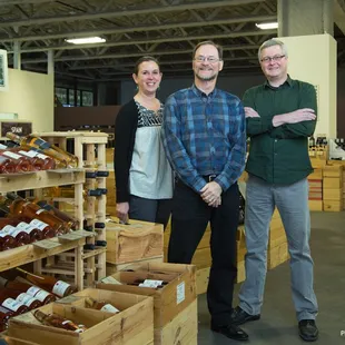 three people standing in front of a wine rack