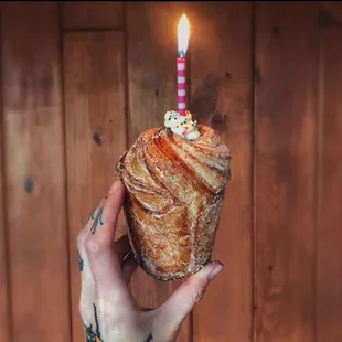 a hand holding a pastry with a lit candle