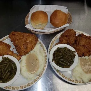 two plates of fried chicken, mashed potatoes and green beans