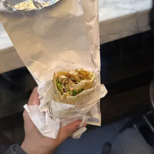 a person holding a sandwich wrapped in foil