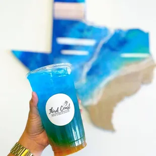 a hand holding a blue drink in front of a map of texas