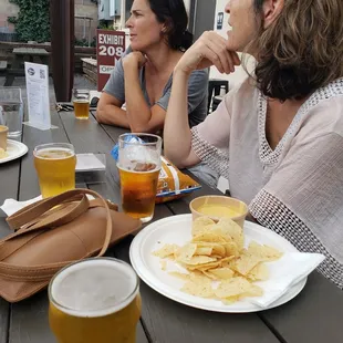 two women sitting at a table with beer and chips