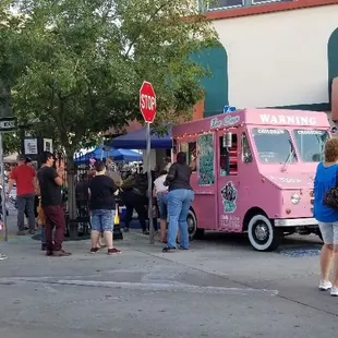 a crowd of people standing in front of a pink ice cream truck
