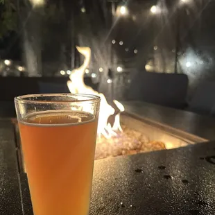 a glass of beer in front of a fire pit