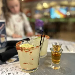 a little girl sitting at a table with a glass of margarita
