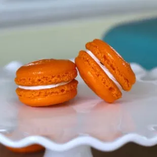 two orange macarons on a cake plate