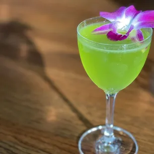 a green cocktail with a purple flower