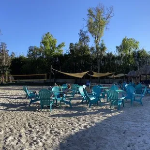 a sandy beach with blue chairs and a hammock