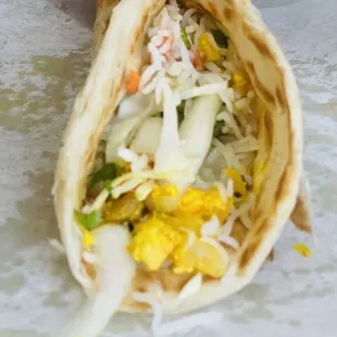 a hand holding a pita filled with vegetables