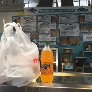 Bag of food and mango Fanta with the menu in the background