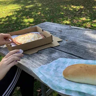 a person sitting at a picnic table with a box of pizza