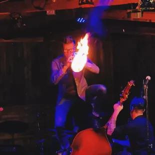 trumpet player playing with trumpet on fire, standing on a cello