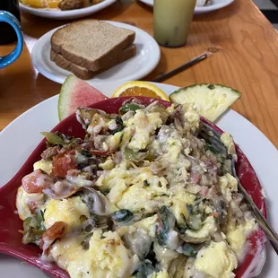 Combo skillet with scrambled eggs, ham, bacon, tomatoes, bell peppers, mushrooms over red potatoes with country sausage gravy